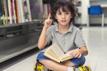 Little child boy reading a book and finger pointing up.
