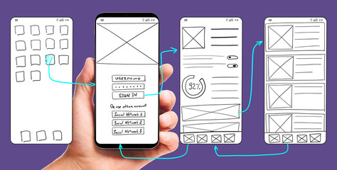 UI development. Male hand holding smartphone with wireframed user interface screen prototypes of a...