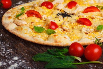Close up chicken Italian pizza with melted mozzarella, red cherry tomatoes and green basil on a brown table decorated by mushrooms, mozzarella and cherry