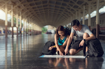 Fototapeta na wymiar Asian couple sitting planing for traveler trip at train station and looking the map on floor.