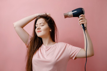 young smiling woman with  hairdryer in hands on pink background