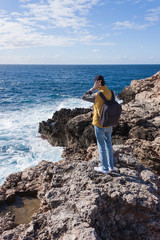 man tourist in yellow vest with backpack on rock cliff in Malta