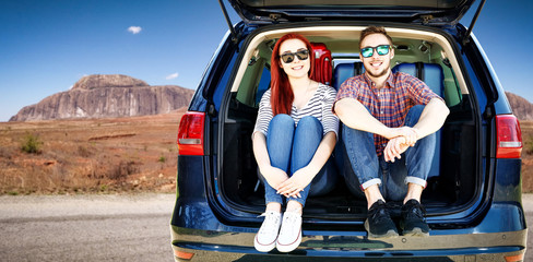 Summer car trip on USA road. Two young people and big blue car with suitcase. Free space for your decoration. 