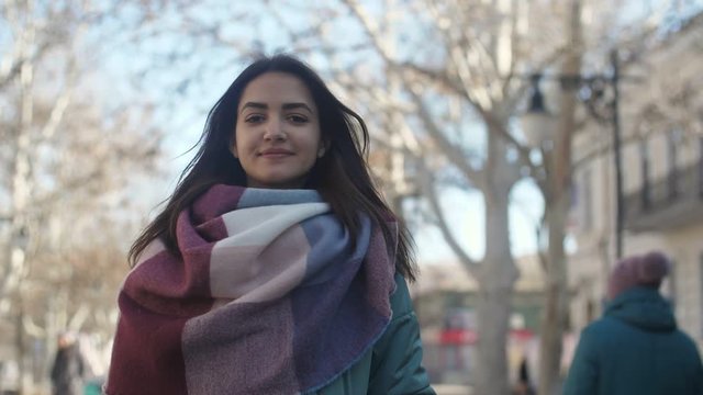 Attractive girl in striped scarf smiling slightly in a street in winter in slow motion  