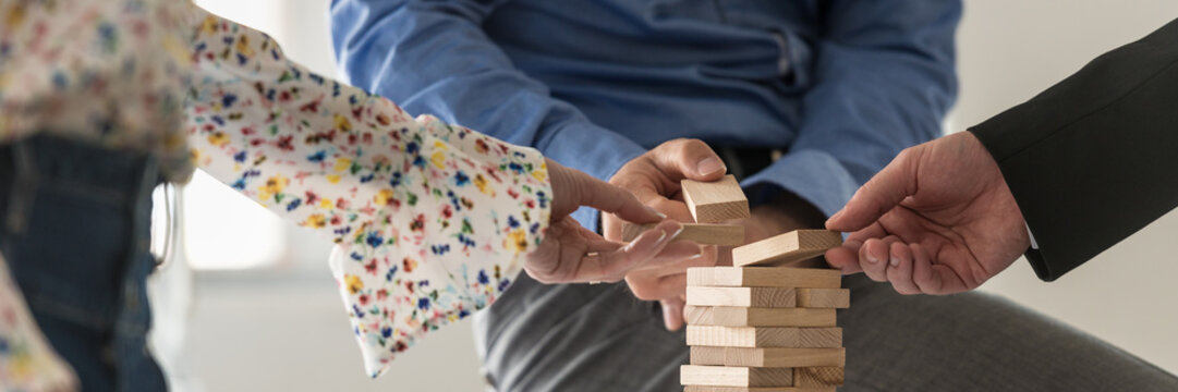Wide view image of three business people making a tower of wooden pegs