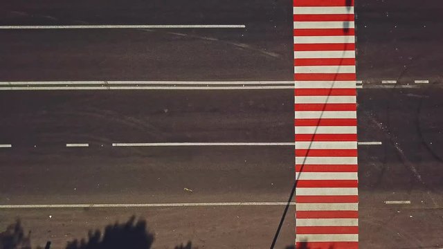 Pedestrian crossing with red and white stripes on the road and cars going by outdoors. Vertical stripes on the road to show drivers the approach of zebra crossing. Camera motion left