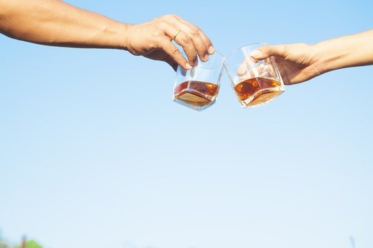 Two friends clink glasses of whisky drink alcoholic beverage together on blue sky background