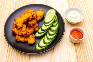Chicken fried (nuggets) homemade on black plate with two sauces - mayonnaise and hot spicy sauce. On wooden background