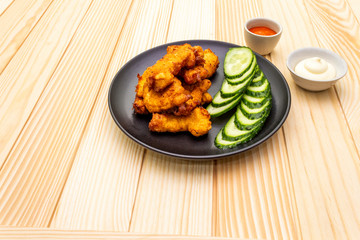 Chicken fried (nuggets) homemade on black plate with two sauces - mayonnaise and hot spicy sauce. On wooden background