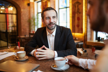 Portrait of handsome mature  businessman talking to partner during meeting in cafe, copy space