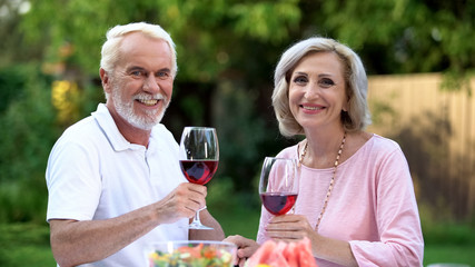 Beautiful senior couple looking at camera, holding wine glasses, dating website