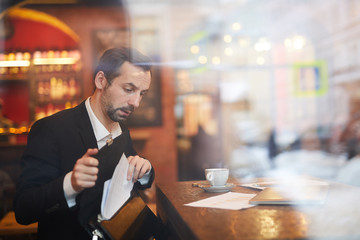 Portrait of mature businessman working at table in cafe shot from behind glass, copy space