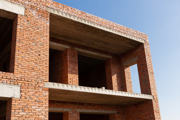 a fragment of an unfinished house of red brick against a blue sky, the concept of real estate, investment in construction