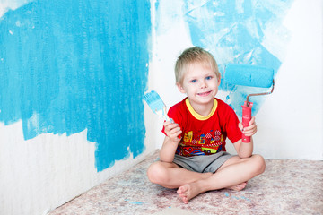 Fototapeta premium Cute blue-eyed blond pretty boy of five years in the red t-shirt makes repair paints the wall in blue roller