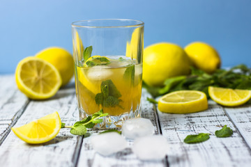 Summer refreshing drink in a glass. Traditional cold sweet-sour lemonade with lemon, mint and ice cubes on a gray wooden table.