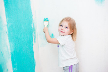 blonde blue-eyed little girl three years doing repairs in the apartment, fun paints the wall by roller / brush in blue