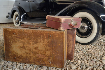 Old suitcases on rubble next to side wheels of vintage car