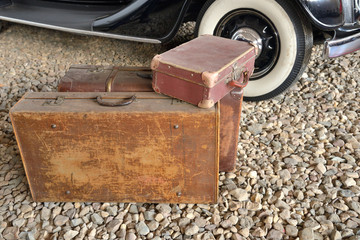 Old suitcases on rubble next to side wheels of vintage car