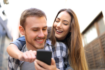 Happy couple piggybacking checking smart phone