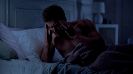 Fototapeta premium Young man suffering migraine, rubbing his temples, having bad sleep, stress