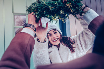Wife wearing warm hat taking Christmas wreath for decorating house - Powered by Adobe
