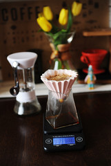 Alternative coffee brewing. Pink ceramic dripper with paper filter. Electronic scale. Yellow tulips on the background