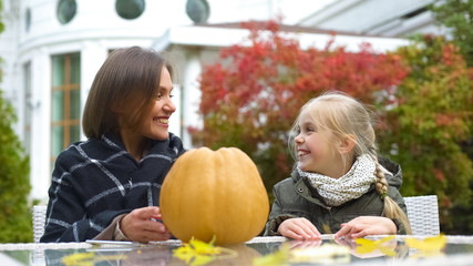 Mom and girl preparing pumpkin for party, sitting on backyard, happy moments