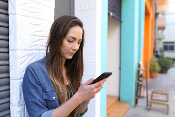 Serious girl using smart phone standing in the street