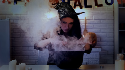 Mysterious young woman in witch costume cooking potion, preparing for Halloween