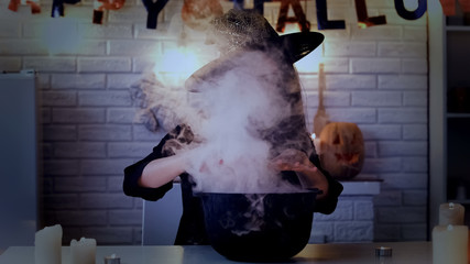 Scary witch making magic potions in her pot with white smoke, Halloween eve