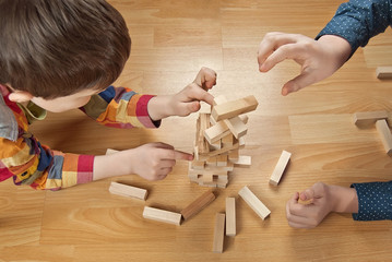 Children are played by the designer on the floor. Hands close-up build a wooden tower.