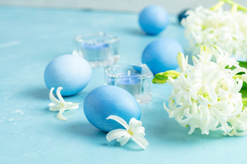 Easter eggs, candles and white hyacinth on a blue concrete