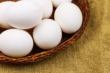 White chicken eggs in wicker basket on sackcloth background