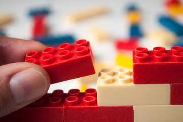 closeup of hand of man playing with plastic bricks construction on white background