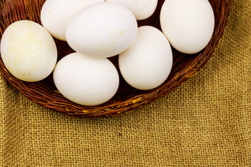 White chicken eggs in wicker basket on sackcloth background