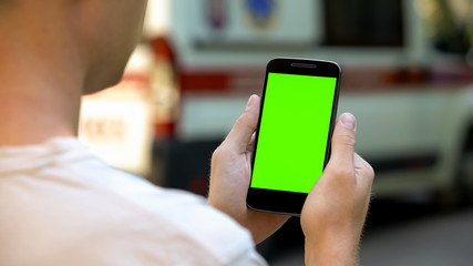 Patient using cellphone to read test results, ambulance on background, closeup
