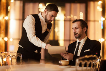 Portrait of handsome mature businessman reading menu in luxury restaurant talking to waiter, copy...