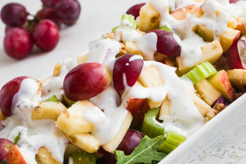 Waldorf salad with apples, celery, grapes, walnuts and arugula and dressing on white plate, closeup