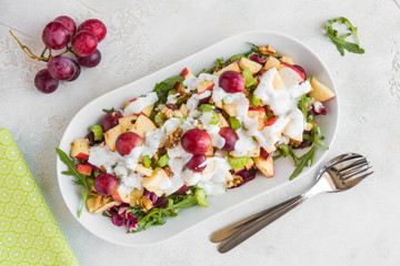 Waldorf salad with apples, celery, grapes, walnuts and arugula on white plate, top view