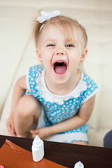 cute smiling baby 3 years old blonde-haired, blue-eyed shears out paper and sticks on paper