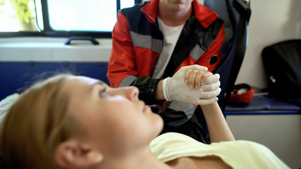 Emergency doctor holding patient hand in ambulance, medical care, moral support