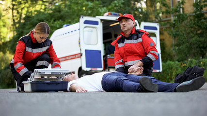 Doctor checking pulse of man lying on road, heart problems, low sugar blood