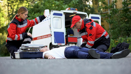 Ambulance service staff care for patient on road, putting intravenous equipment
