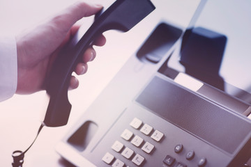 Male hand,  IP phone with buttons and big display, laptop on the office table. Ip telephony and...