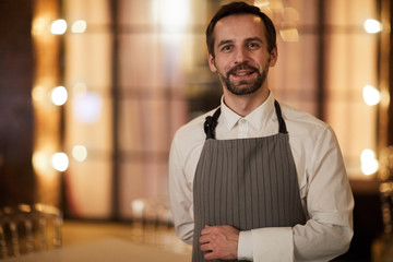 Waist up portrait of mature waiter wearing apron posing in luxury restaurant or cafe, copy space
