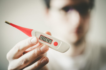 Man is holding a fever thermometer in his hand, blurry face