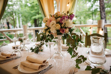 A big bouquet and a lot of cutlery are standing on the table. Restauraunt terrace on the background.