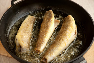 Fish is fried in a pan. Cook a dish of cod fish in a skillet over butter. Fried fish in cast iron.