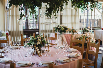 A table with a pink tablecloth, a lots of cutlery and a flower bouquet on it. Restauraunt terrace at the background.