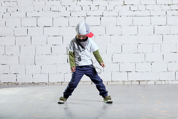 Child model posing in young rapper clothes. Cool kid boy dancing break dance.Hip-hop style. studio, brick wall background.
